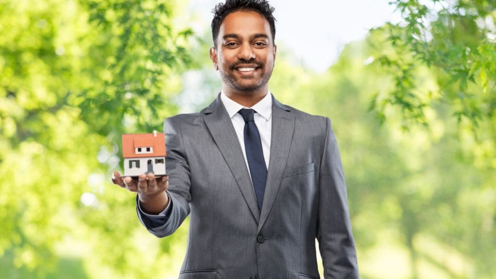 A professional real estate agent presenting a selling a house sign in front of a beautiful suburban home.